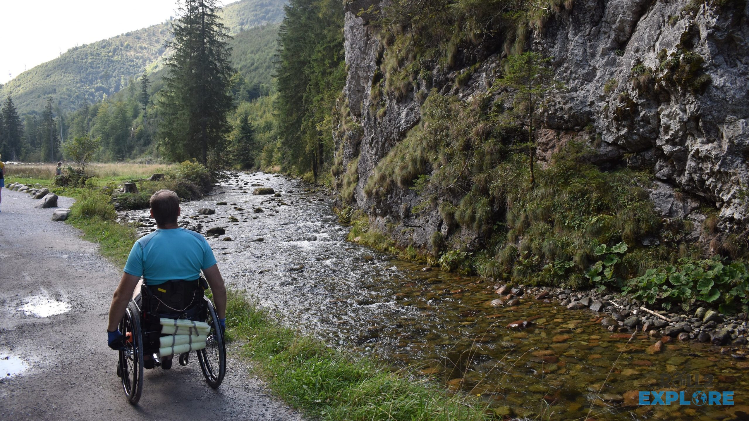 Nick in a wheelchair in Koscieliska Valley on a dirt trail next to a creek