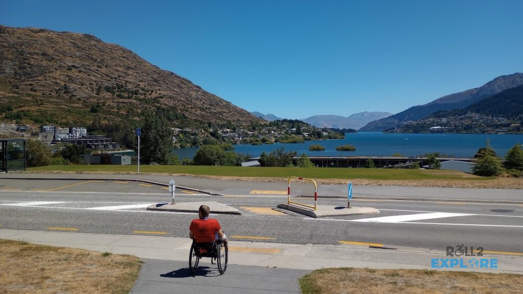 Nick in a wheelchair in front of a street looking at the Wakatipu lake and Queenstown
